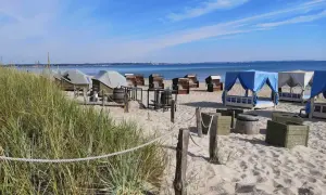 Scharbeutz Strand: Strandkörbe, Liegen unter blauen und weißen Zelten, Tische und Fässer am Sandstrand.