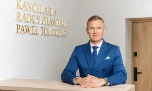Mężczyzna w niebieskim garniturze za ladą, za nim napis "KANCELaria Radcy Prawnego Paweł Tołoczko".