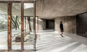 Interior moderno con paredes y techos de hormigón texturizado. Una mujer camina por los suelos de hormigón pulido, proyectando sombras.