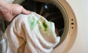 Hand hält Handtuch mit grünen Grasflecken vor einer Waschmaschine. Zeit, Grasflecken entfernen!