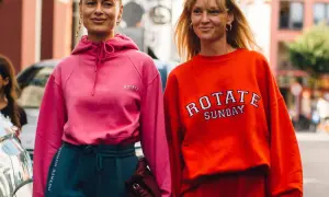 Dwie kobiety w sportowych stylizacjach, idealnych na podróż. Różowa bluza i granatowe dresy lub pomarańczowa bluza i czerwone dresy to świetny pomysł, jak ubrać się do samolotu.
