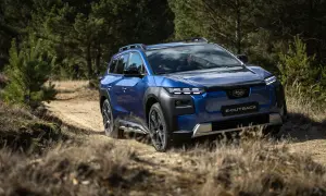 Niebieskie Subaru E-Outback pokonuje piaszczystą drogę wśród drzew. Jazda Subaru po bezdrożach.