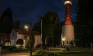 Nocna panorama z latarnią morską Rozewie, budynkami i ceglanym kominem.
