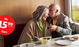 Ein verliebtes Rentnerpaar genießt eine Bahnfahrt mit Essen und Wein. Ab 15,99 Euro können auch Sie so die Reise erleben.