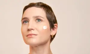 Une femme au regard pensif, avec une touche de crème solaire avant ou après crème hydratante sur la joue.