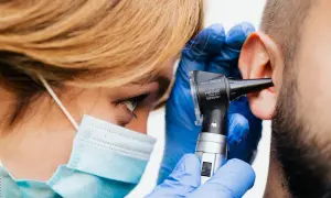Médico examina oído con otoscopio. Si sufres de dolor de oído, consulta a un profesional para saber qué tomar.