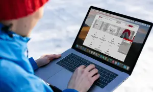 Osoba w czerwonej czapce i niebieskiej kurtce korzysta z laptopa, na ekranie którego widoczna jest strona internetowa KRD.