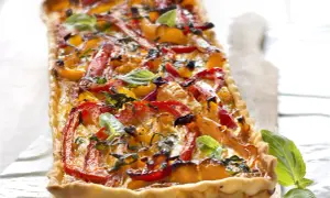 Tarte rectangulaire aux poivrons rouges et jaunes grillés, garnie de basilic frais. Un délice coloré et savoureux.