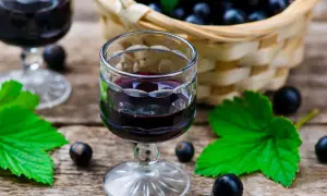 W kieliszku wino z porzeczek czarnych, obok koszyk pełen owoców i liście.