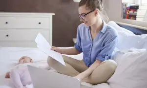 Kobieta na macierzyńskim pracuje przy laptopie, podczas gdy dziecko śpi obok.