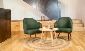 Två mörkgröna fåtöljer i skandinavisk inredningsstil, med ett runt träbord och en kopp kaffe.