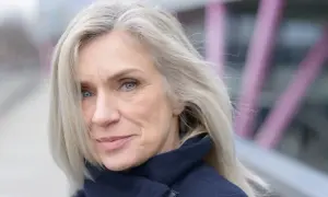Donna con capelli biondo cenere, un sorriso discreto e occhi azzurri. Nonostante i capelli bianchi, il suo look è curato, quasi a voler camuffare capelli bianchi con un'eleganza naturale.