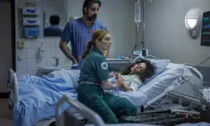 En ambulanssjuksköterska håller en patients hand medan en läkare ser på. Scen från en vaka serie.