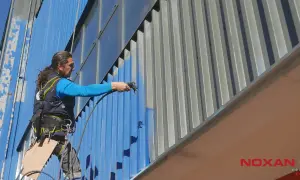 Pracownik na wysokości wykonuje malowanie na mokro stalowej elewacji budynku.