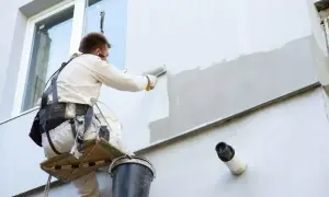 Pracownik na wysokościach maluje elewację budynku, używając wałka.