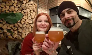 Coppia brinda con birra artigianale alla huisbrouwerij de halve maan. Sfondo rustico con legna e mattoni.