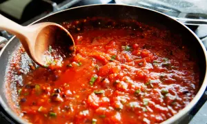Gęsty, aromatyczny sos do spaghetti gotuje się na patelni. Drewniana łyżka miesza pomidorową masę z ziołami.