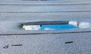 Pfützen auf der Dachpappe spiegeln den Himmel. Feuchtigkeit unter Dachpappe deutet auf ein Problem hin.