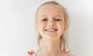 Uśmiechnięta dziewczynka z blond włosami, kiedy rosna 6 ząbków, pokazuje swoje nowe mleczaki.