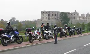 Motocykliści i ich maszyny na tle ruin zamku.