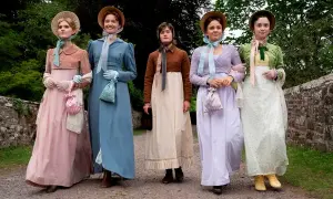 Pięć kobiet w strojach z epoki, przypominających rodzeństwo Jane Austen, spaceruje po kamienistej ścieżce.