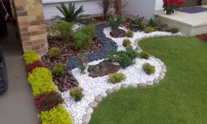 Un jardín moderno con grava blanca, rocas, plantas verdes y flores rojas, diseñado por paisajistas de jardines.