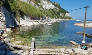 La spiaggia della Scalaccia, con le sue acque cristalline e le scogliere bianche, accoglie bagnanti e piccole imbarcazioni.