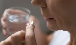Dłoń trzyma tabletkę aspiryny i szklankę wody.
