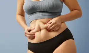 Kobieta z rumianymi paznokciami chwyta fałd skóry na brzuchu, ukazując sylwetkę typu "skinny fat".