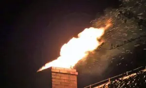 Jasny płomień wydobywa się z ceglanego komina, a w powietrzu latają iskry. To niebezpieczny pożar sadzy w kominie.