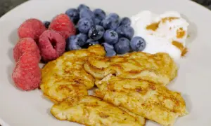 En tallrik med gyllene pannkakor, färska hallon, blåbär och en klick yoghurt med kanel. Perfekt för diabetes mat recept.