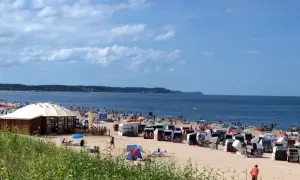 Plaża nad Bałtykiem z leżakami, parasolami i ludźmi kąpiącymi się w morzu.