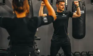 Ein Trainer zeigt Muskelaufbau nach Intensivstation. Eine Frau im EMS-Anzug trainiert.