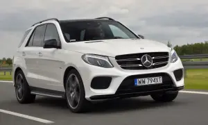 Biały Mercedes GLE 400d z czarnym dachem pędzi po drodze. Kierowca w okularach prowadzi auto.