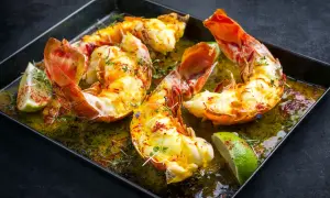 Langoustes grillées dans un plat avec du citron vert et des herbes.