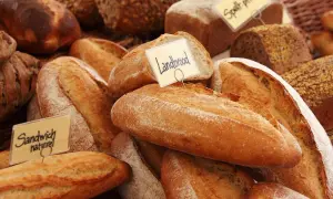 Różnorodne pieczywo, w tym bochenki z etykietami "Landbrood" i "Sandwich naturel". Zastanawiasz się, czym smarować chleb przed pieczeniem, by uzyskać chrupiącą skórkę?