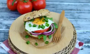 Pyszny burger z jajkiem sadzonym, rukolą, pomidorem i czerwoną cebulą na desce z drewna.