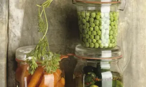 Ein Glas mit Erbsen einkochen, daneben ein Glas mit Karotten und ein Glas mit Gewürzgurken. Eine Karotte liegt obenauf.