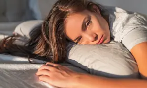 Donna sdraiata sul cuscino, con sguardo stanco e capelli lunghi. Potrebbe soffrire di anemia sideropenica.