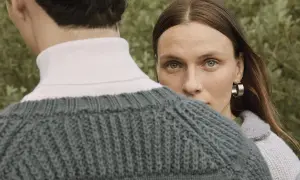 Kobieta z kolczykiem w uchu spogląda zza ramienia mężczyzny w swetrze. To styl marki Filippa K.
