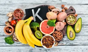Frutta e verdura che mostrano dove si trova la vitamina K2: banane, broccoli, avocado, pomodori, uva passa, mandorle, semi di zucca, patate, funghi, nocciole.
