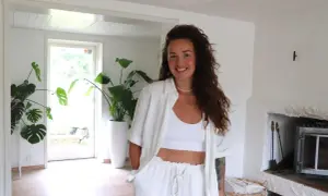 Nathalie Steffner ler mot kameran i ett ljust rum med stora gröna växter och en öppen spis.