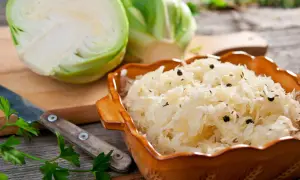 Schüssel mit Sauerkraut, Gewürzen und frischem Weißkohl. Ein Messer und Petersilie deuten auf ein traditionelles Sauerkraut Rezept hin.