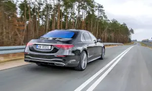 Czarny Mercedes S400d 4Matic sunie po drodze wśród drzew.