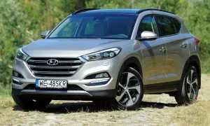 Srebrny Hyundai Tucson III na tle zieleni. Poznaj różne wersje wyposażenia tego wszechstronnego SUV-a.