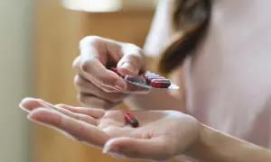 Dłoń wyjmuje kapsułkę z blistra. Jedna kapsułka leży na otwartej dłoni. To może być suplement diety, np. pikolinian chromu.