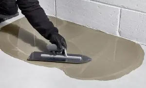 Ręka w rękawiczce wygładza świeżą wylewkę betonową kielnią.