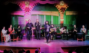 Un cantante sevillano flamenco baila en el escenario, acompañado por guitarristas y palmeros.