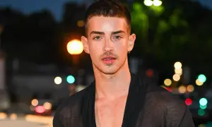 Uomo con capelli spettinati, sguardo intenso e un leggero sorriso. Indossa una veste trasparente nera.