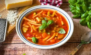 Herzhaftes rezept minestrone original mit viel Gemüse und Pasta, garniert mit frischem Basilikum. Daneben Parmesan und ein Löffel.